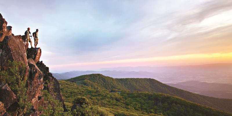 Two hikers on a cliff overlooking the mountain views in Shenandoah National Park in Virginia USA